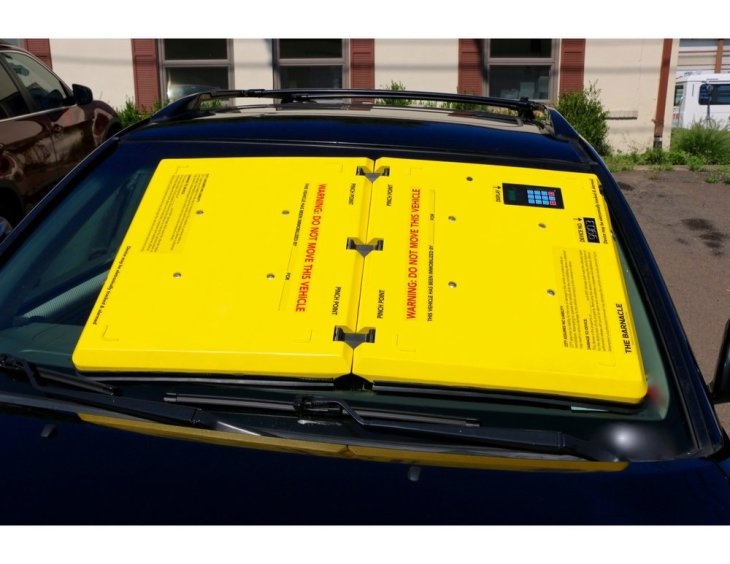 Yellow parking barnacle device installed on a vehicle windshield which immobilizes the vehicle.